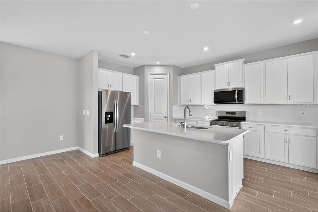 A modern kitchen features white cabinetry, stainless steel appliances, a center island, and wood-look flooring — 13018 SUNSEED STREET, PARRISH, FL