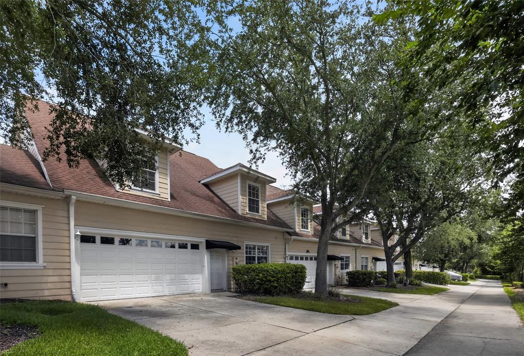 A row of tan townhouses with white garage doors and dormer windows under large trees — 332 NAUTICA MILE DRIVE, CLERMONT, FL