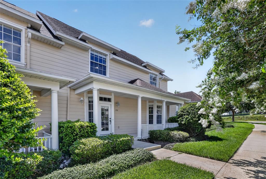 A two-story beige townhouse with a covered front porch, white columns, and manicured landscaping — 332 NAUTICA MILE DRIVE, CLERMONT, FL