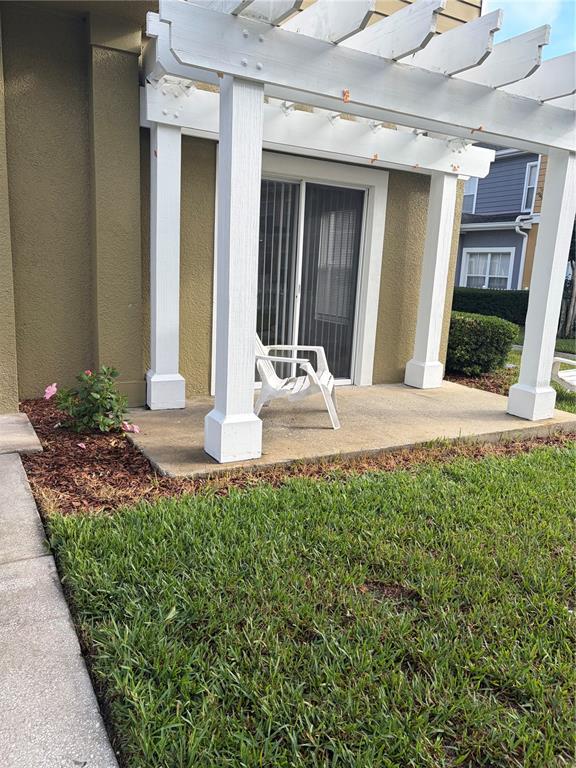 A concrete patio with a white pergola and a single chair sits outside a sliding door — 2610 LODI CIRCLE UNIT 102, KISSIMMEE, FL