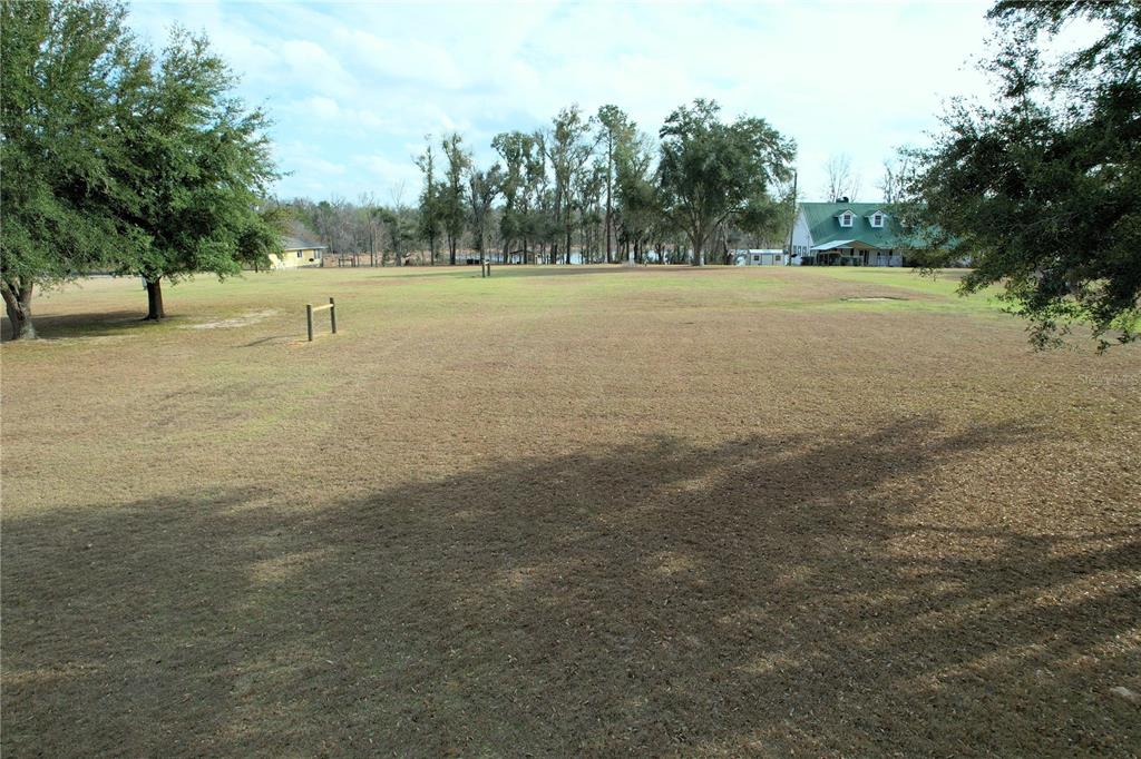 A large, grassy field with trees and a house in the background — 00 NW BUR OAK PLACE, JENNINGS, FL