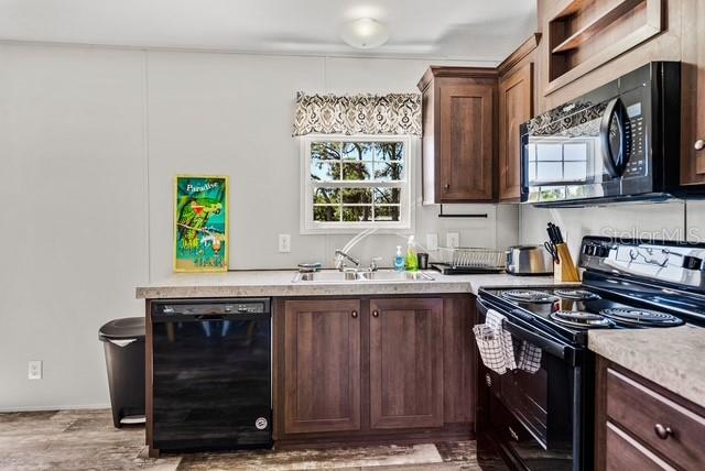 A kitchen features dark wood cabinets, a black dishwasher, and a microwave above the stove — 14418 STEPHENS ROAD, PORT CHARLOTTE, FL