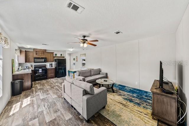 A living room with wood-look flooring, a grey sofa, and an open-concept kitchen — 14418 STEPHENS ROAD, PORT CHARLOTTE, FL