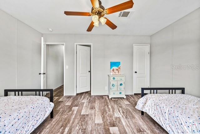 A bedroom features two twin beds, wood-look flooring, a ceiling fan, and two white doors — 14418 STEPHENS ROAD, PORT CHARLOTTE, FL