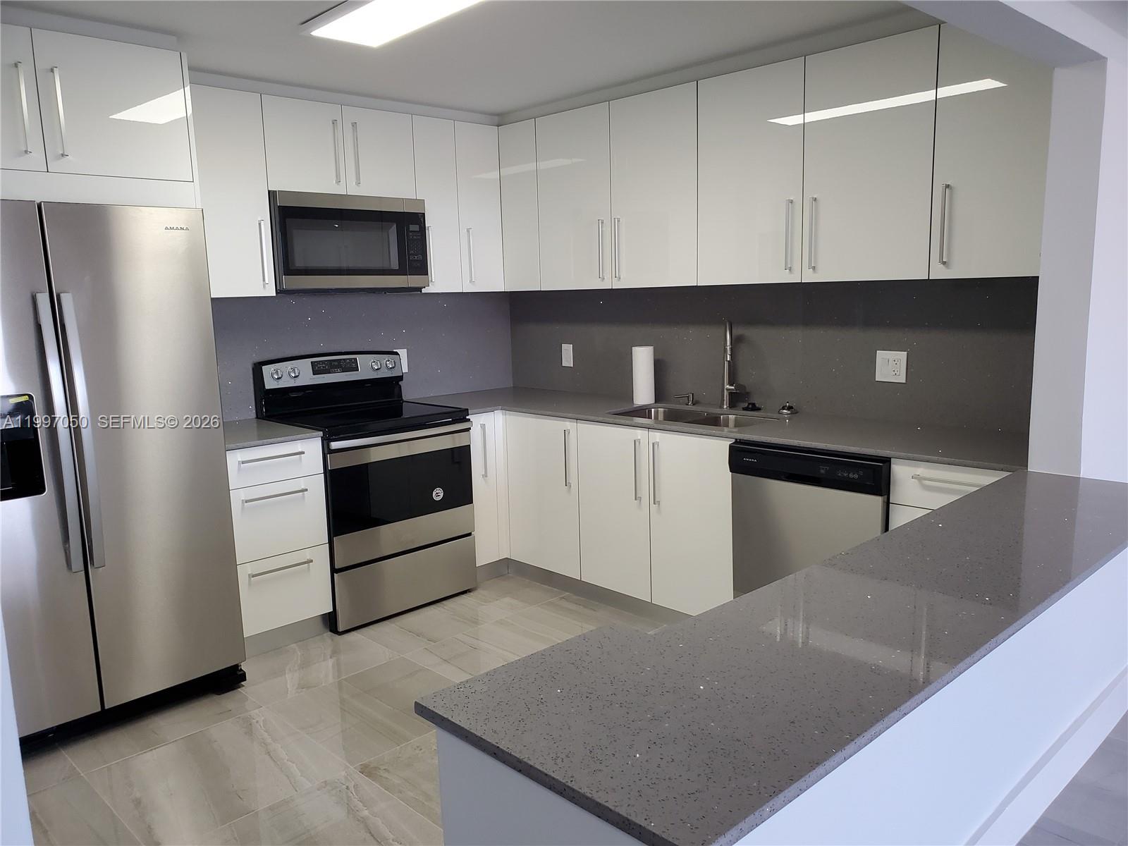 A modern kitchen features white cabinets, stainless steel appliances, and gray quartz countertops — 13499 Biscayne Blvd # 1105, North Miami FL 33181, NORTH MIAMI, FL
