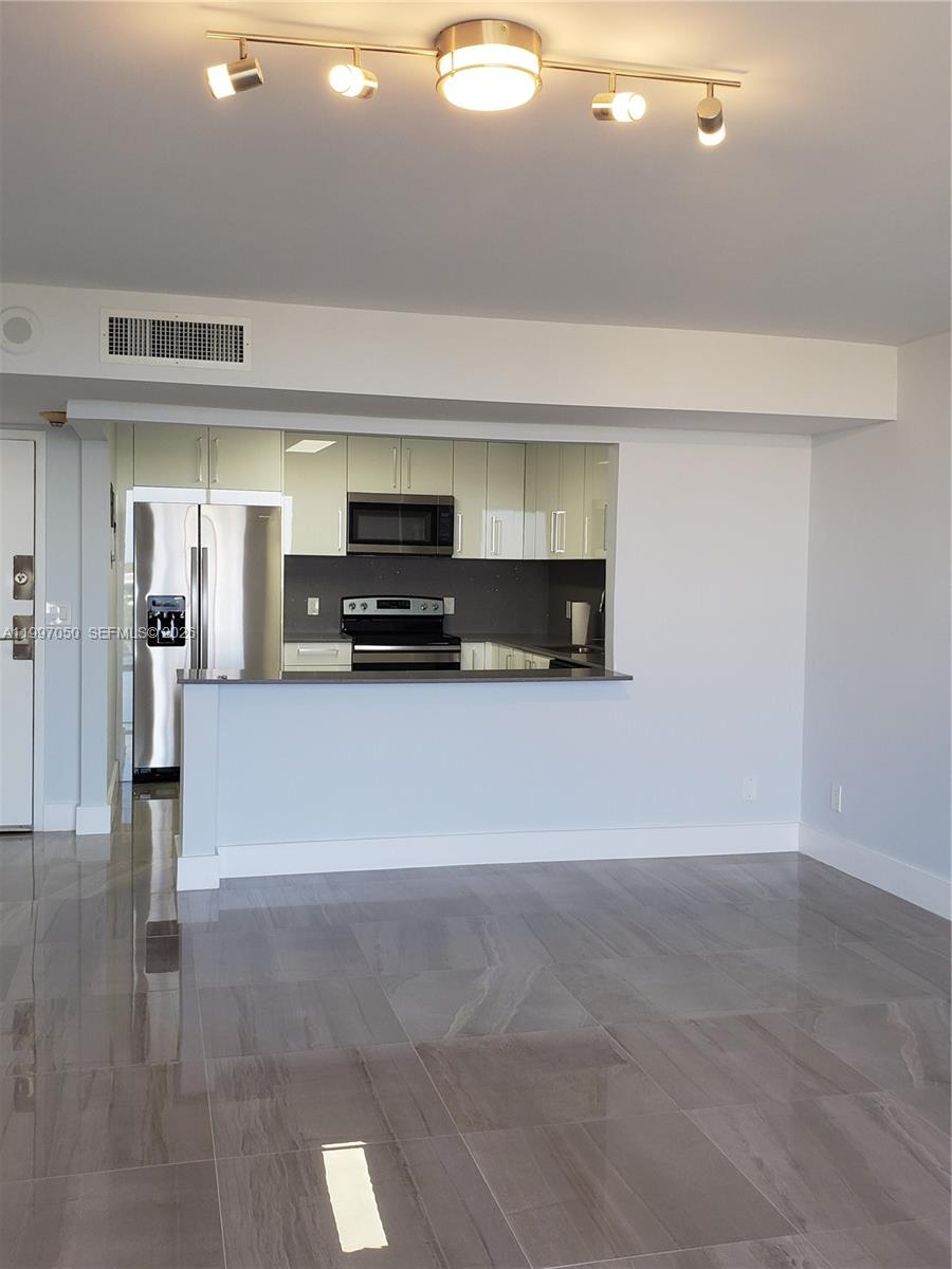 A kitchen with stainless steel appliances and white cabinets overlooks a living area with tile — 13499 Biscayne Blvd # 1105, North Miami FL 33181, NORTH MIAMI, FL