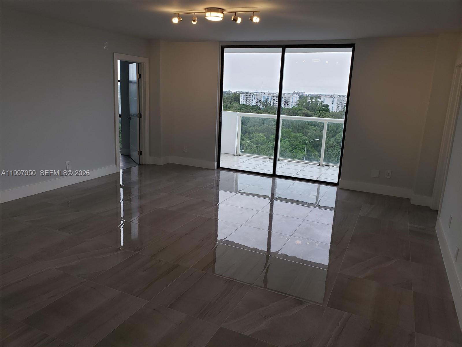 An empty room features large glossy floor tiles, a sliding glass door, and a balcony — 13499 Biscayne Blvd # 1105, North Miami FL 33181, NORTH MIAMI, FL