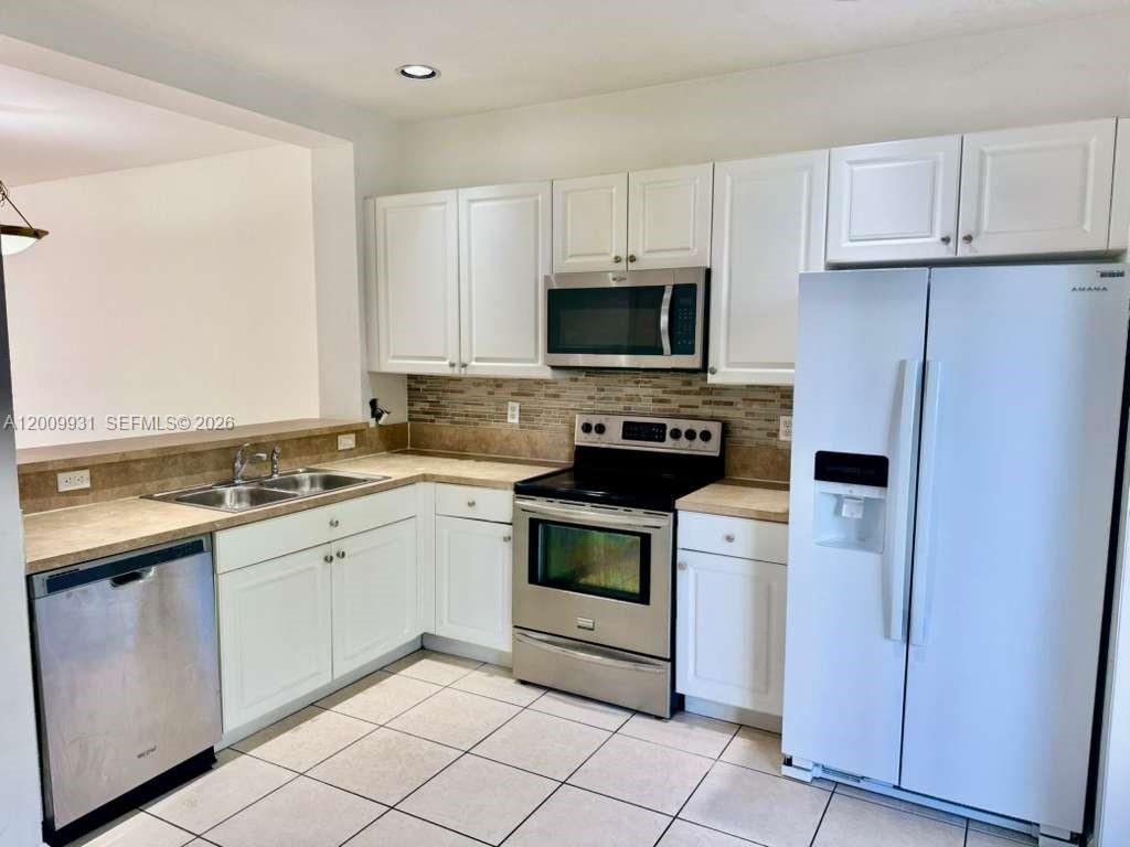 A kitchen features white cabinets, stainless steel appliances, tile flooring, and tan countertops — 669 NW 42nd Ave, Plantation FL 33317, PLANTATION, FL