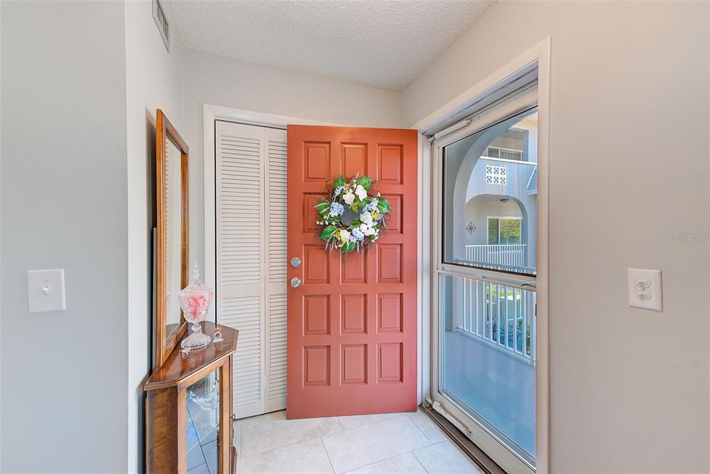 An entryway features a terracotta-colored front door, a glass storm door, and a wooden console — 2229 AMERICUS BOULEVARD W UNIT 25, CLEARWATER, FL