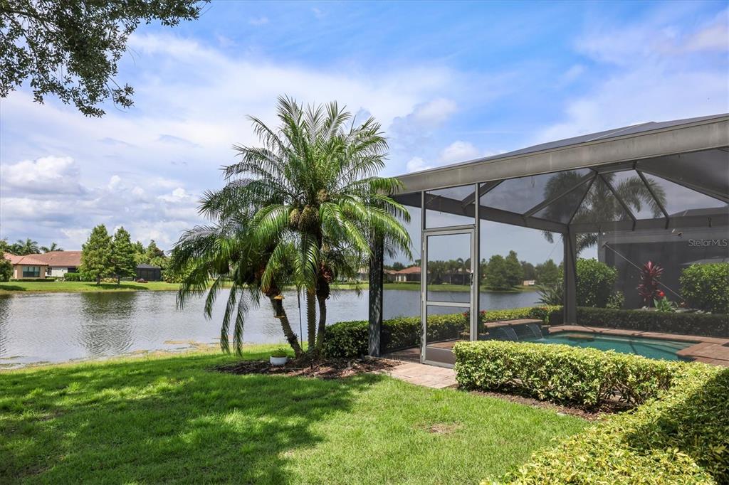 A screened-in pool patio overlooks a lake with a palm tree in the foreground — 12749 FONTANA LOOP, BRADENTON, FL