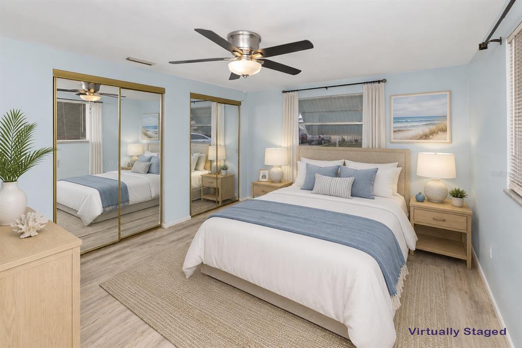 A bedroom with light blue walls, a queen bed, mirrored closets, and wood-look flooring — 3128 KILBURN ROAD, HOLIDAY, FL
