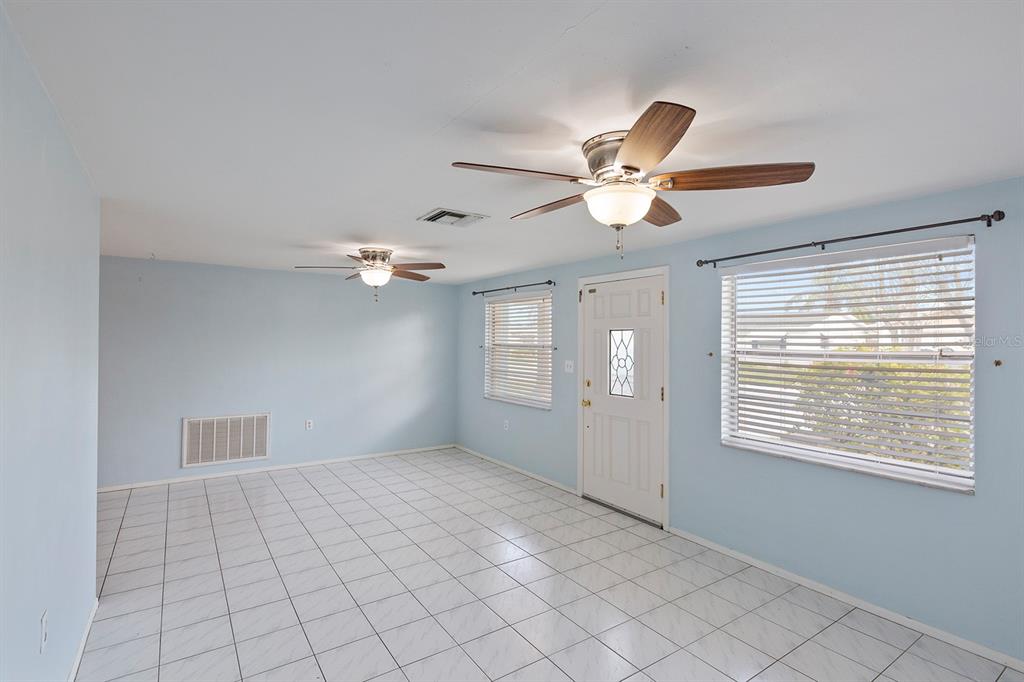 A room with light blue walls, white tiled floors, two ceiling fans, and a front door — 3128 KILBURN ROAD, HOLIDAY, FL
