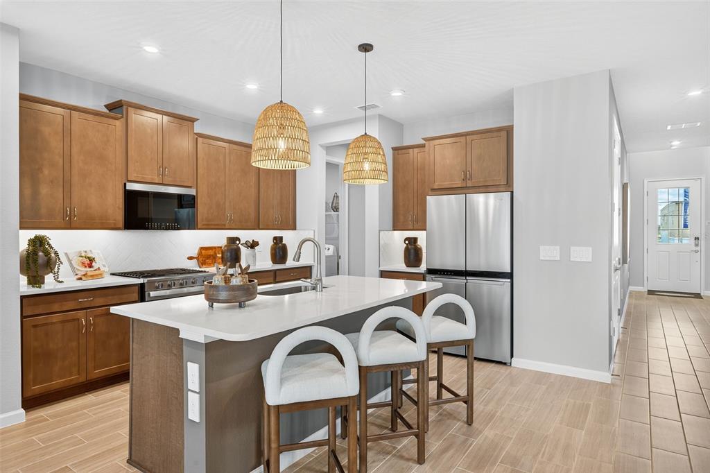 A kitchen features wood cabinets, a white island with three stools, and stainless steel appliances — 1762 SOARING VIDA STREET, PALMETTO, FL