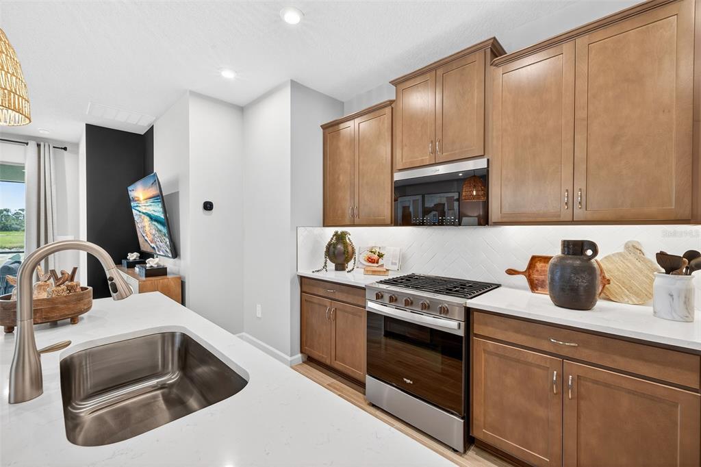 A modern kitchen features wood cabinets, stainless steel appliances, and a white quartz island countertop — 1762 SOARING VIDA STREET, PALMETTO, FL