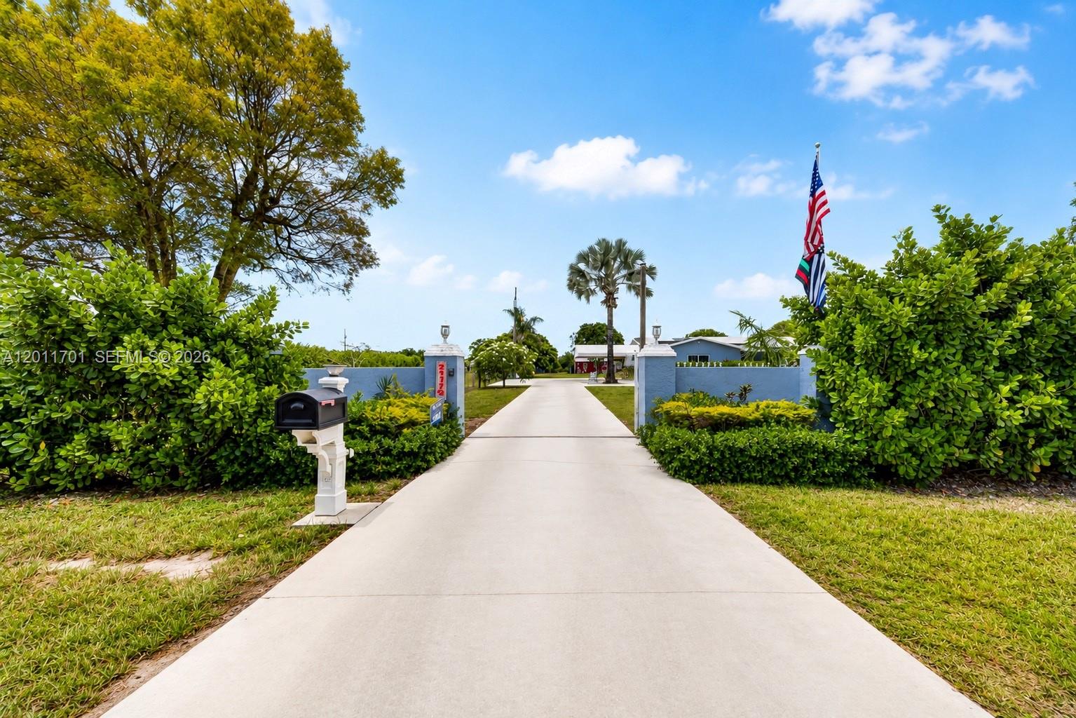 A concrete driveway leads to a gated entrance with a mailbox and an American flag — 21175 SW 232nd St, Miami FL 33170, MIAMI, FL