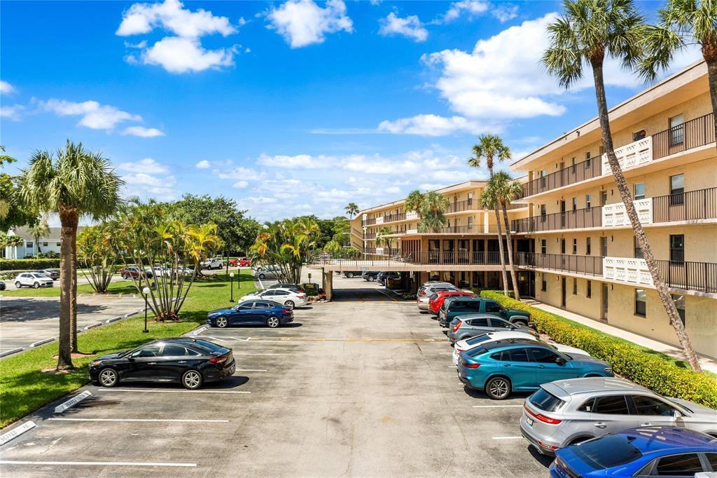 An outdoor parking lot sits in front of a multi-story apartment building with palm trees — 9355 SW 8th Street # 109, Boca Raton FL 33428, BOCA RATON, FL