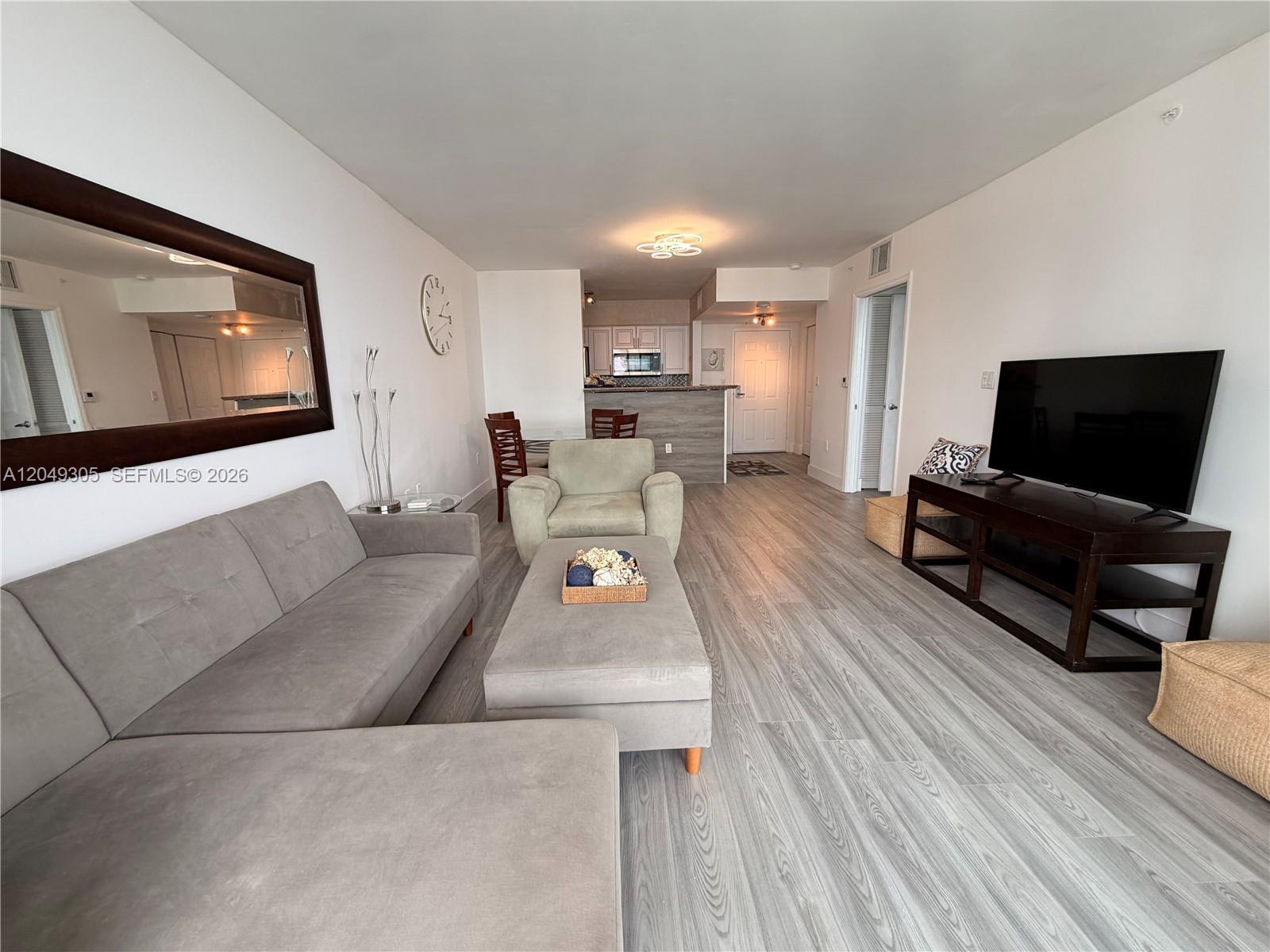 A living room features gray flooring, a sectional sofa, a television console, and an open kitchen — 1155 Brickell Bay Dr # 3405, Miami FL 33131, MIAMI, FL