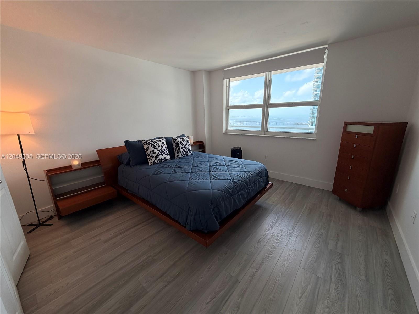 A bedroom features a platform bed, wooden furniture, and a large window overlooking the water — 1155 Brickell Bay Dr # 3405, Miami FL 33131, MIAMI, FL