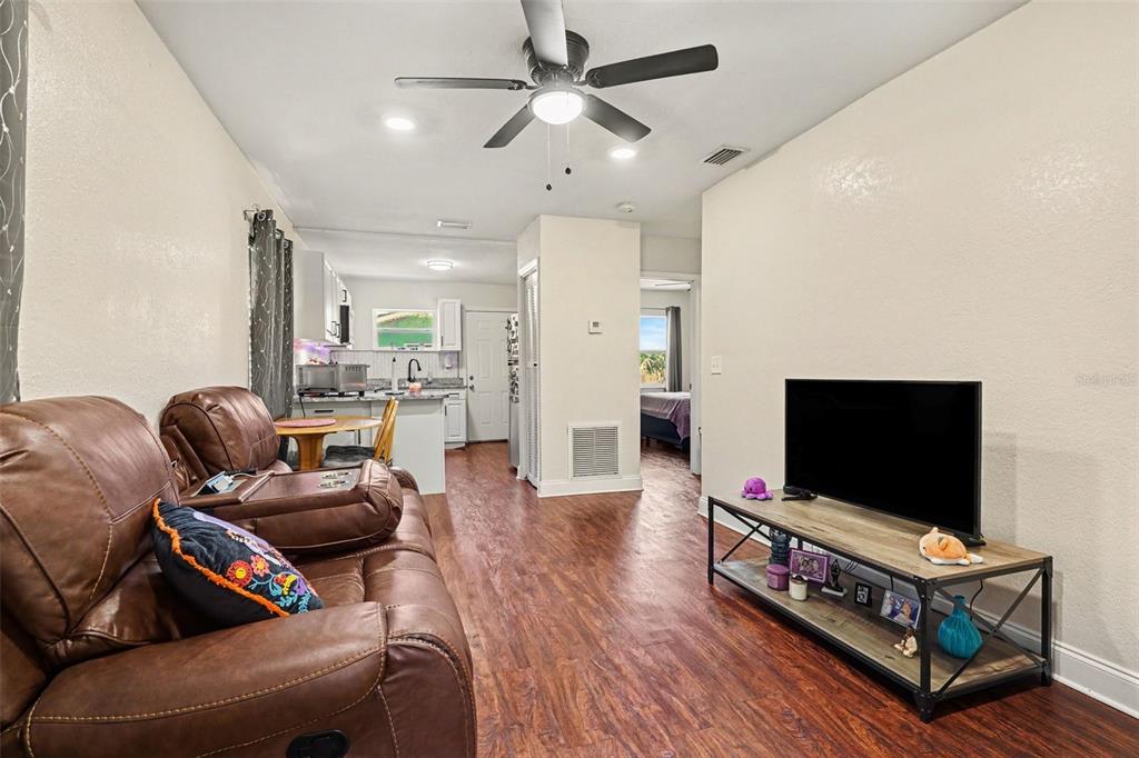 A living room with wood-look flooring, a brown leather sofa, and a television stand — 614 W 6TH STREET, LAKELAND, FL