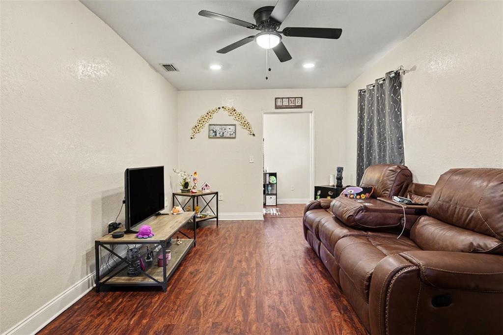 A living room features a brown leather sofa, a television stand, and wood-look flooring — 614 W 6TH STREET, LAKELAND, FL
