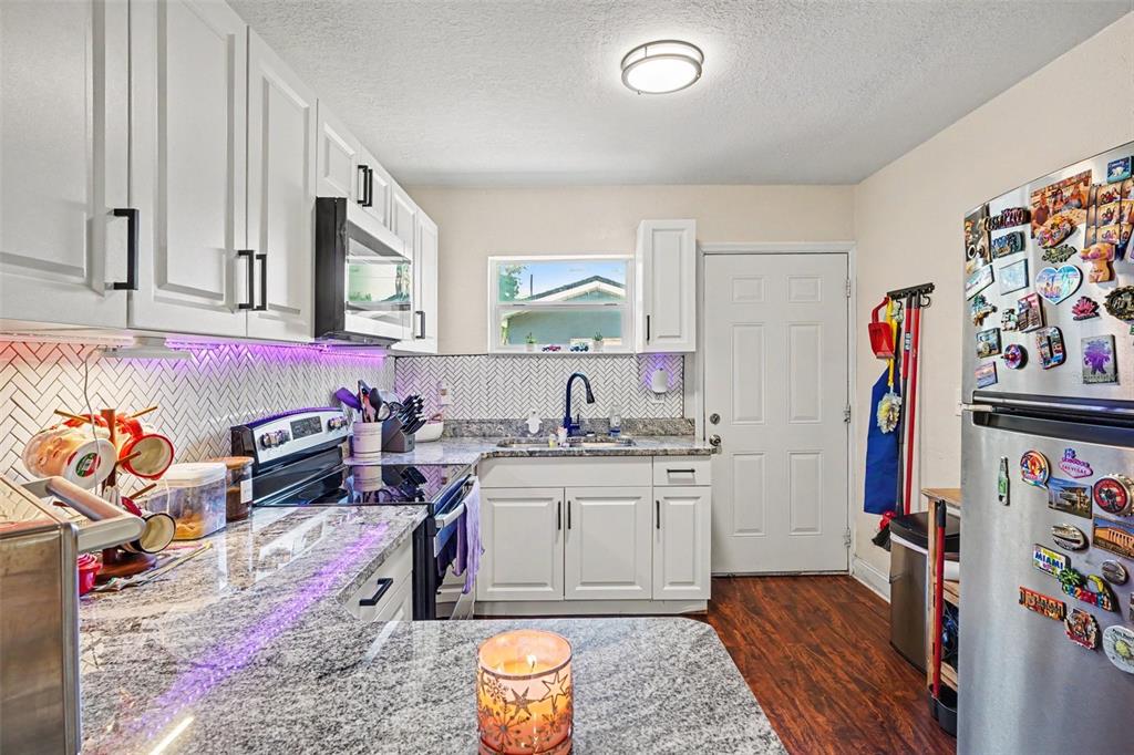A kitchen features white cabinets, granite countertops, a herringbone backsplash, and a stainless steel refrigerator — 614 W 6TH STREET, LAKELAND, FL
