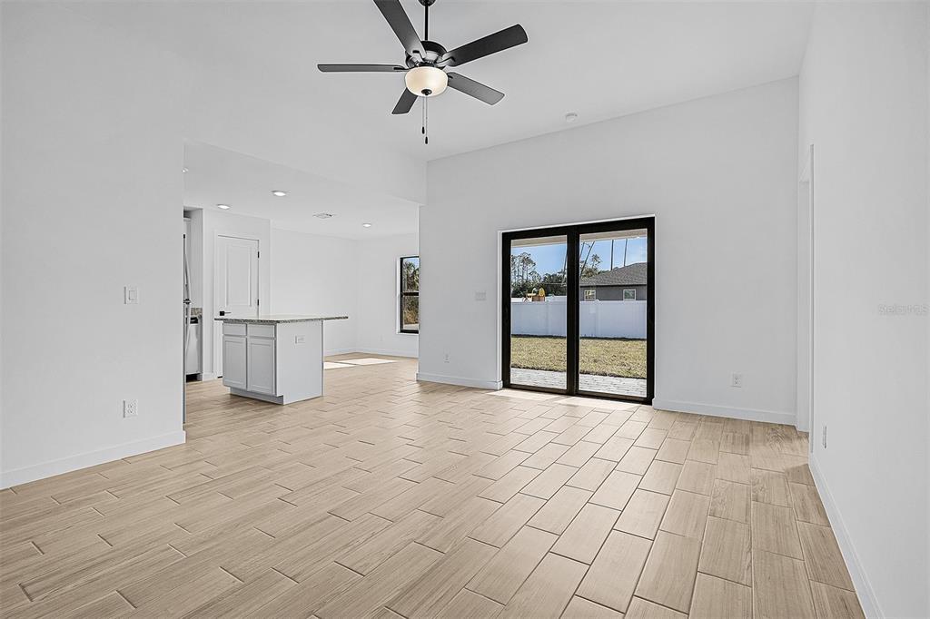 A bright living area with light wood-look tile floors, a ceiling fan, and sliding glass doors — 3560 BELLEFONTE AVENUE, NORTH PORT, FL