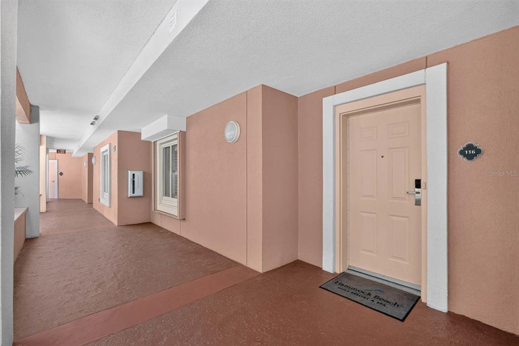 An exterior hallway features a tan door labeled 116 with a resort-branded welcome mat — 200 OCEAN CREST DRIVE UNIT 116, PALM COAST, FL
