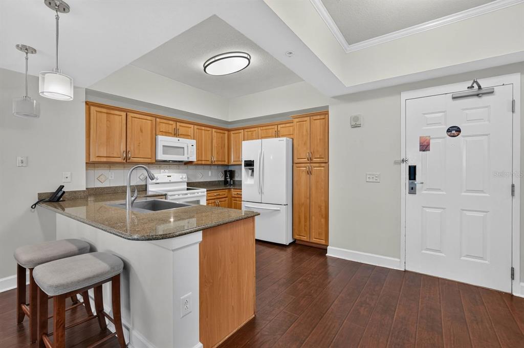A kitchen with wood cabinets, granite countertops, white appliances, and a breakfast bar with stools — 200 OCEAN CREST DRIVE UNIT 116, PALM COAST, FL