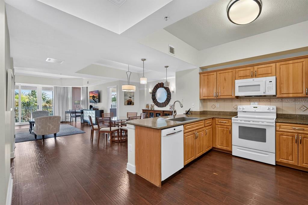 A kitchen with wood cabinets and granite countertops opens into a dining and living area — 200 OCEAN CREST DRIVE UNIT 116, PALM COAST, FL