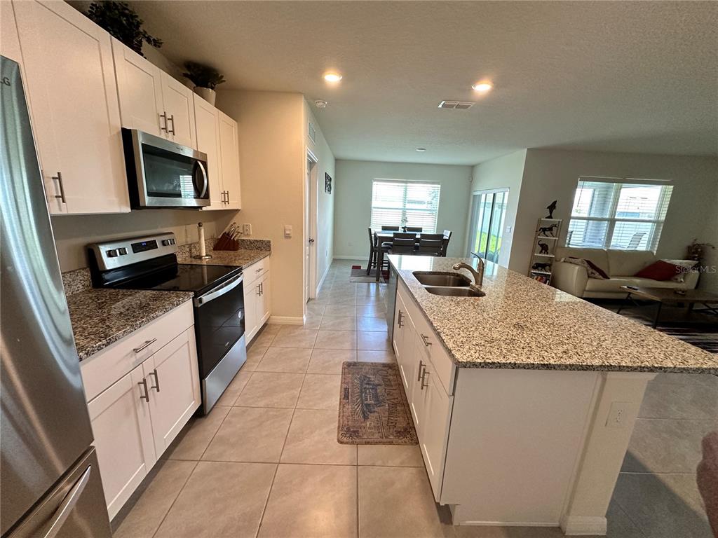 A kitchen with white cabinets, granite countertops, and a center island opens to a dining area — 1855 EGRET MEADOWS AVENUE, KISSIMMEE, FL