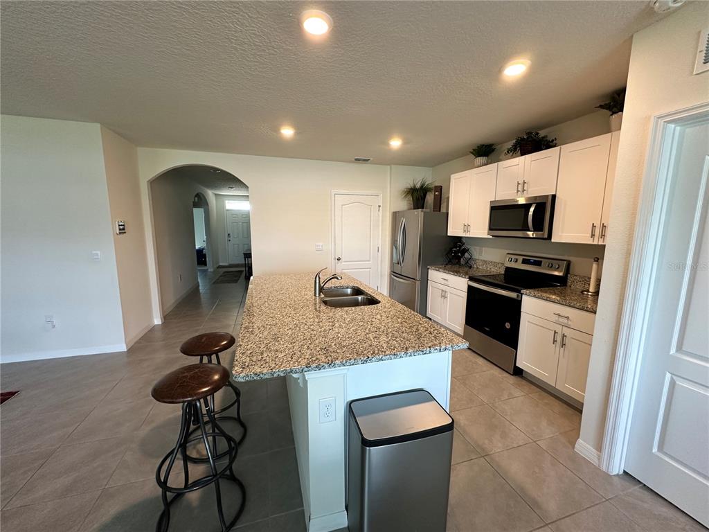 A kitchen features a granite-topped island, white cabinetry, stainless steel appliances, and tile flooring — 1855 EGRET MEADOWS AVENUE, KISSIMMEE, FL