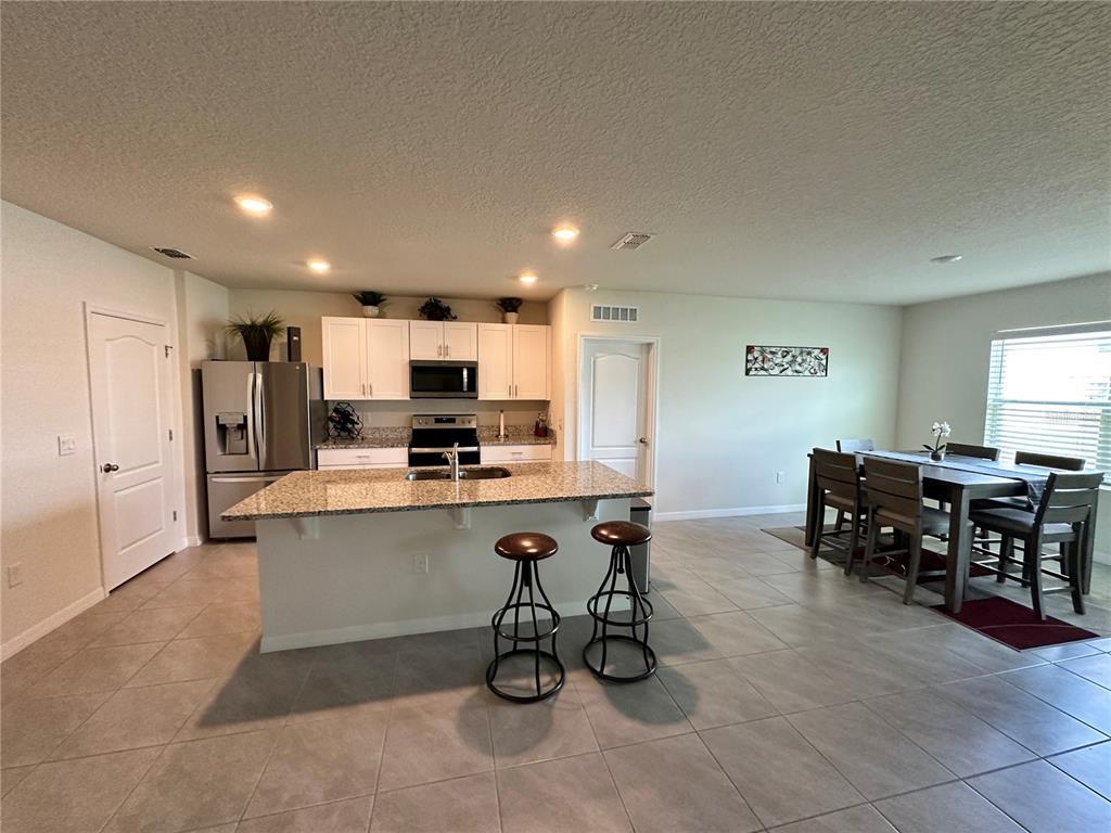A kitchen with a granite-topped island and stools sits adjacent to a dining area — 1855 EGRET MEADOWS AVENUE, KISSIMMEE, FL