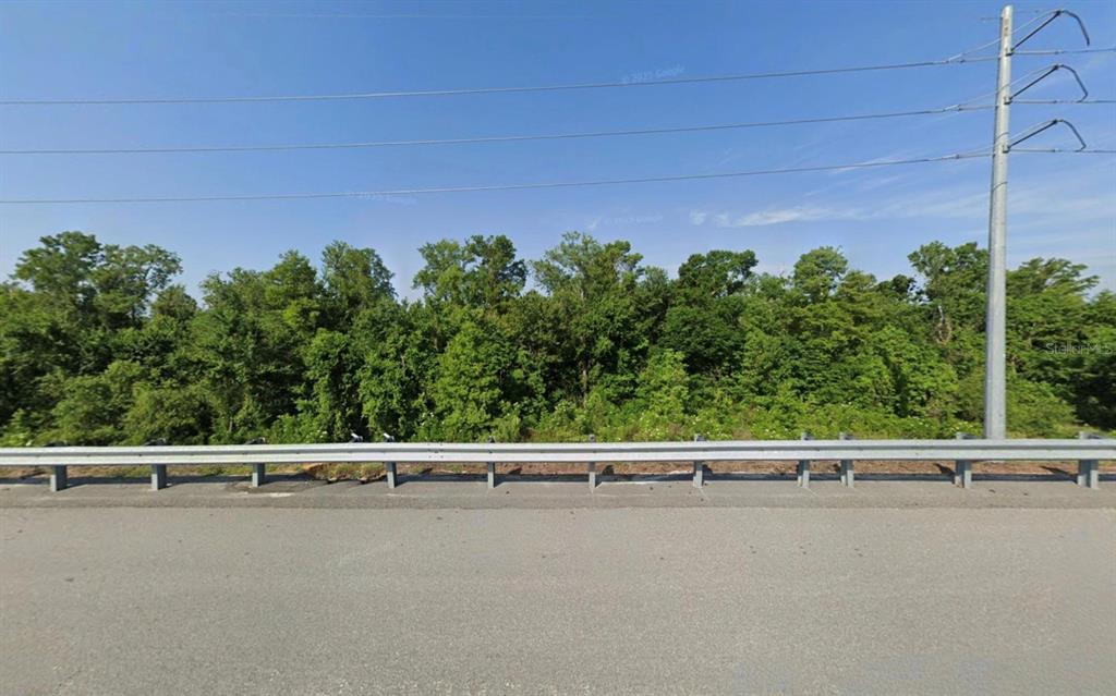 A paved road with a metal guardrail sits in front of a dense treeline — SHELLEY TRAIL, KISSIMMEE, FL