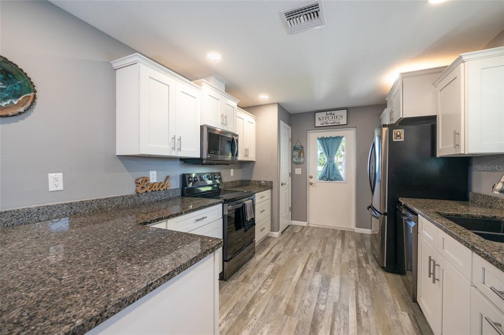 A kitchen with white cabinets, dark granite countertops, stainless steel appliances, and wood-look flooring — 904 S DAYTONA AVENUE, FLAGLER BEACH, FL