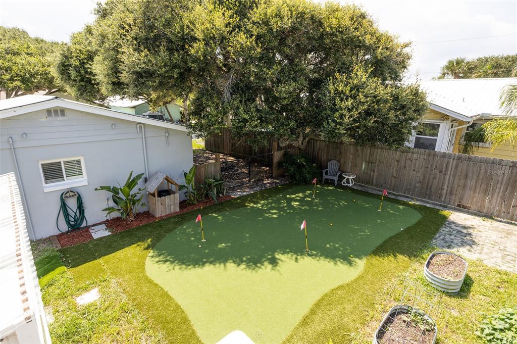 A backyard features a putting green with four holes, a wooden fence, and mature trees — 904 S DAYTONA AVENUE, FLAGLER BEACH, FL