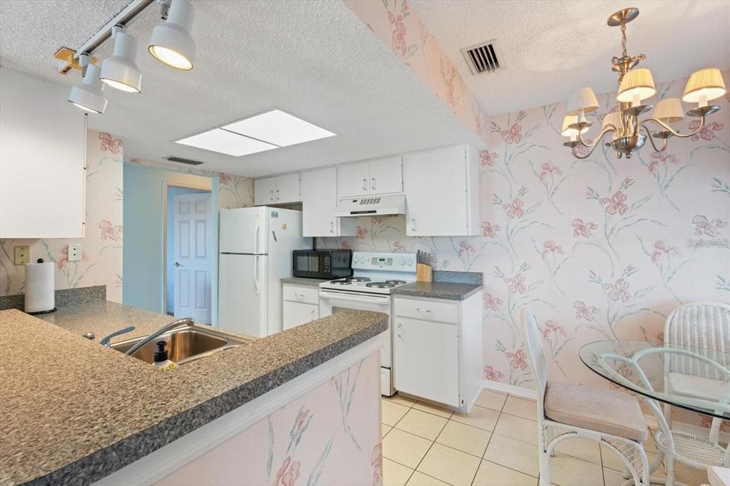 A kitchen with white cabinets, floral wallpaper, a breakfast nook, and a granite-topped peninsula — 312 108TH STREET W, BRADENTON, FL