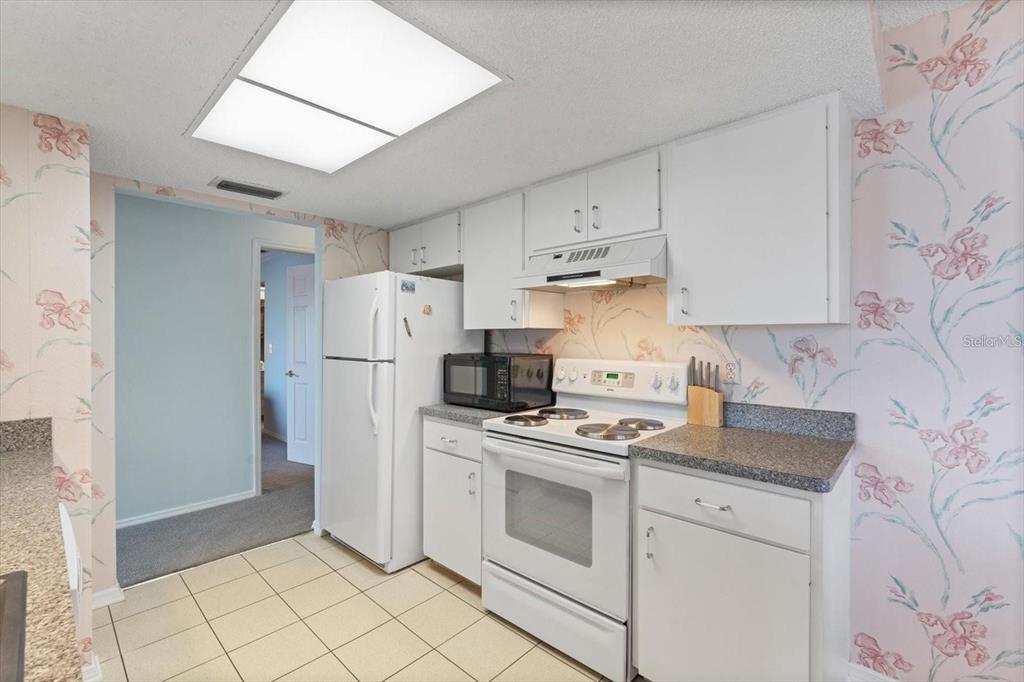 A kitchen features white cabinets, white appliances, speckled countertops, and floral wallpaper — 312 108TH STREET W, BRADENTON, FL