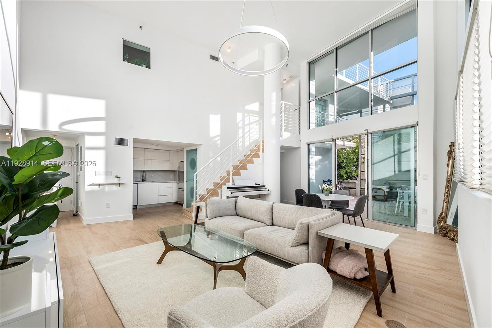 A modern, high-ceilinged living room features a sofa, glass coffee table, and large windows — 221 Jefferson Ave # 2, Miami Beach FL 33139, MIAMI BEACH, FL