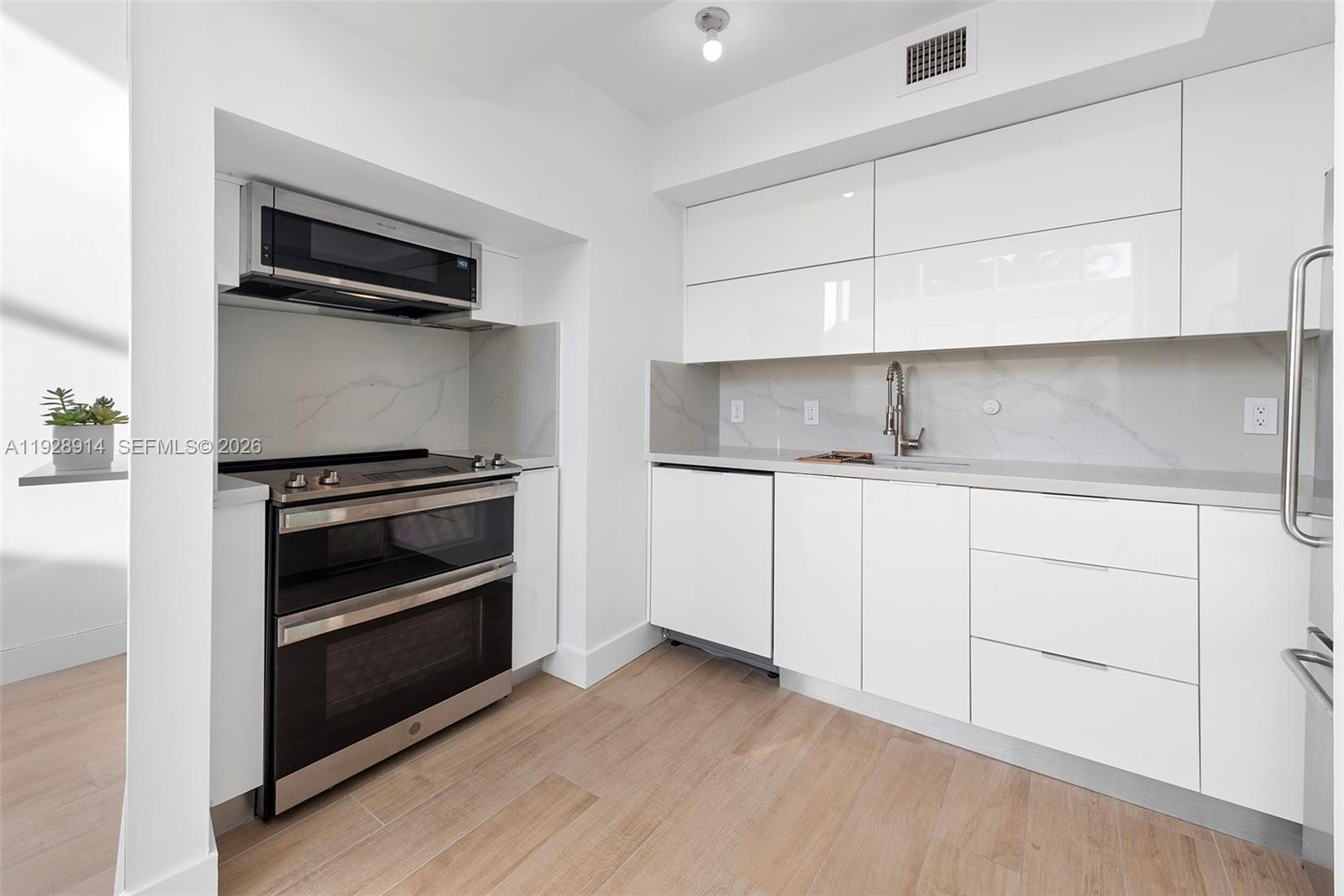 A modern kitchen features white glossy cabinets, stainless steel appliances, and light wood-look flooring — 221 Jefferson Ave # 2, Miami Beach FL 33139, MIAMI BEACH, FL