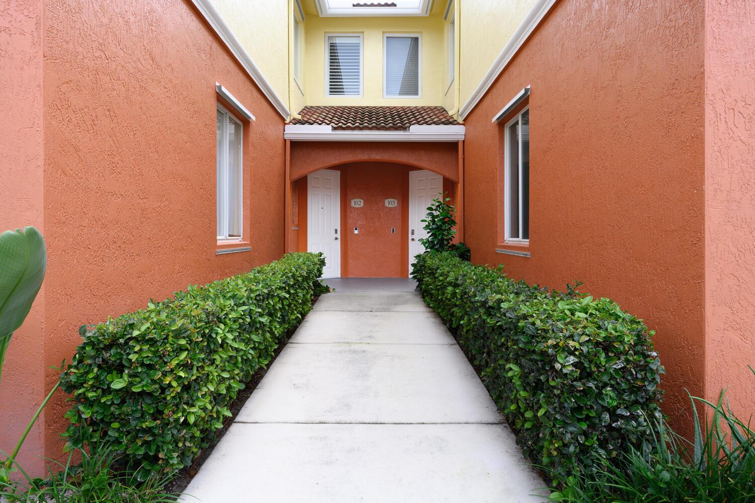 A concrete walkway leads to two adjacent apartment entrances framed by orange stucco walls — 40 SE Sedona Circle # 103, Stuart FL 34994, STUART, FL