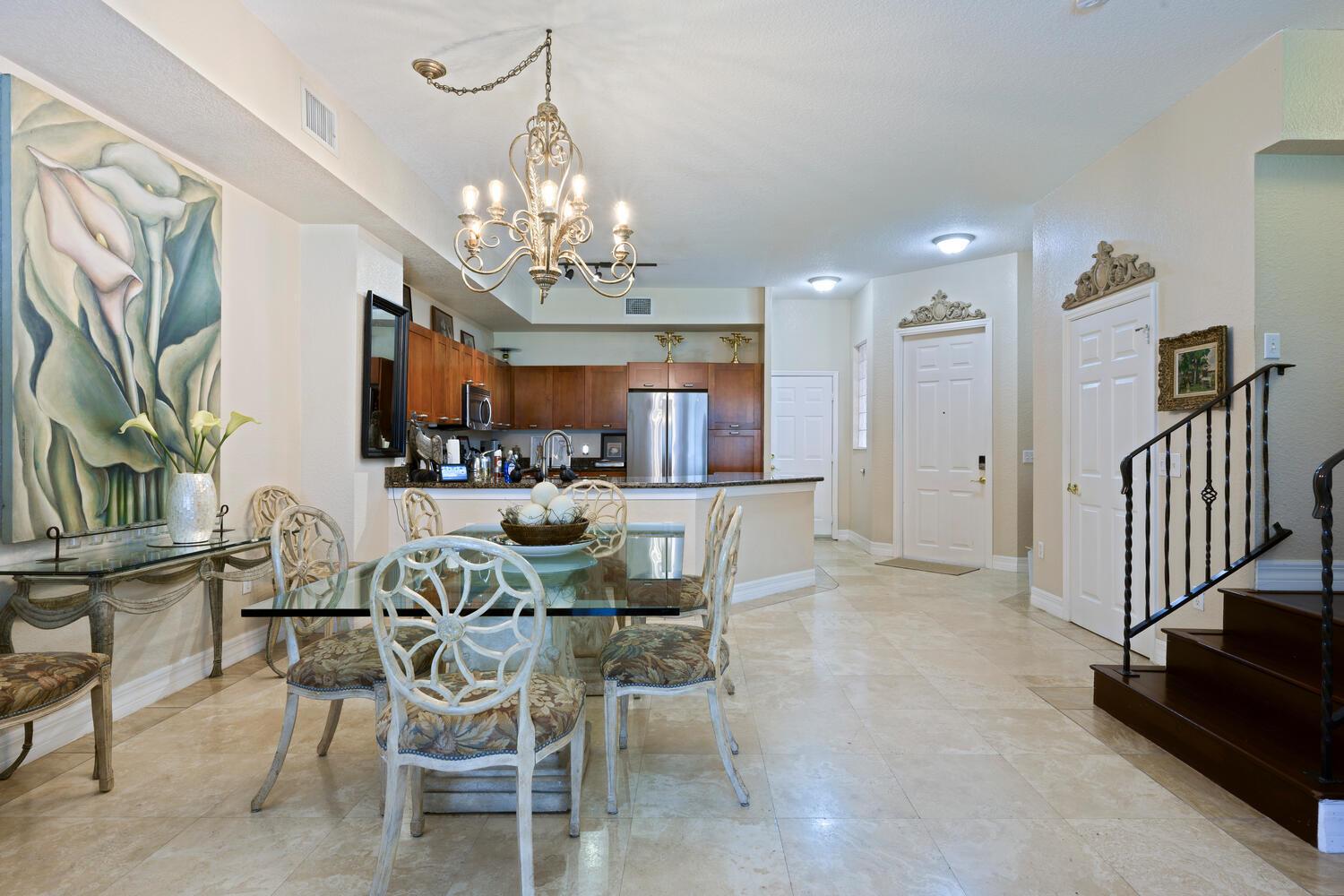 A dining area with a glass table and chandelier sits adjacent to an open kitchen — 40 SE Sedona Circle # 103, Stuart FL 34994, STUART, FL