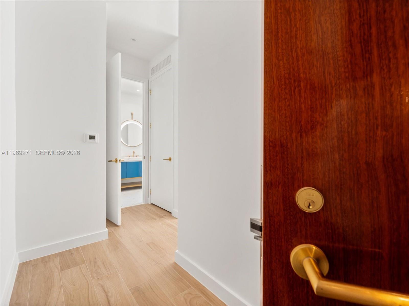 A hallway with light wood-look flooring leads to a bathroom with a blue vanity — 2655 S Bayshore Dr # 1707, Miami FL 33133, MIAMI, FL