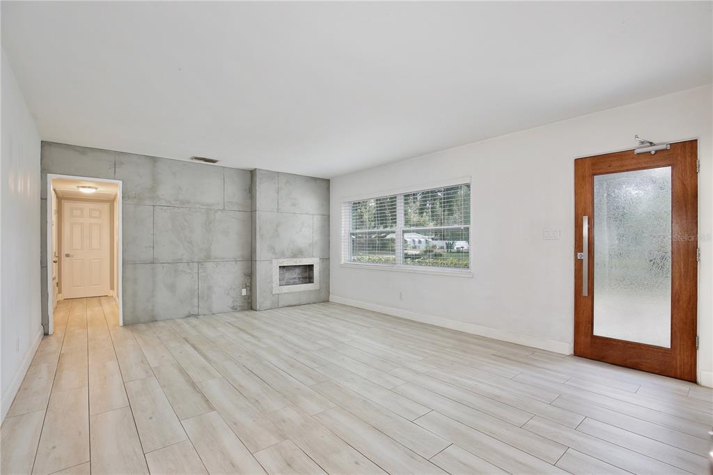 A living room features light wood-look tile floors, white walls, and a concrete-paneled accent wall — 2401 ALBERT LEE PARKWAY, WINTER PARK, FL