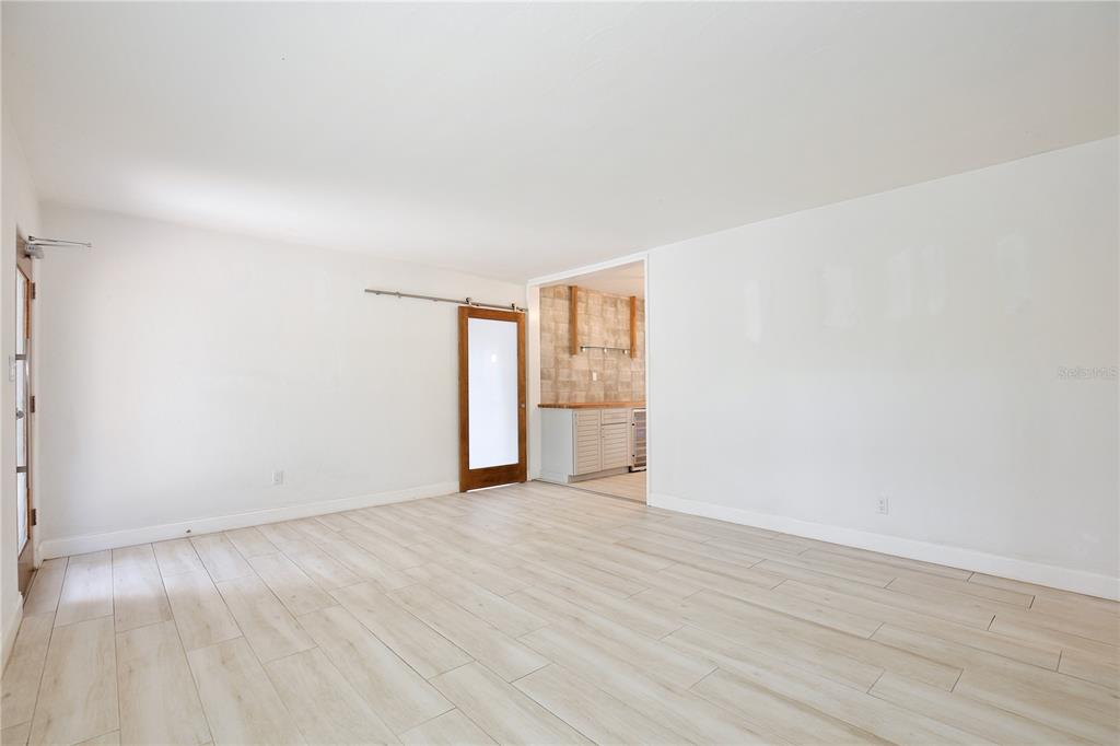 A bright, empty room features light wood-look tile flooring, white walls, and a sliding barn door — 2401 ALBERT LEE PARKWAY, WINTER PARK, FL