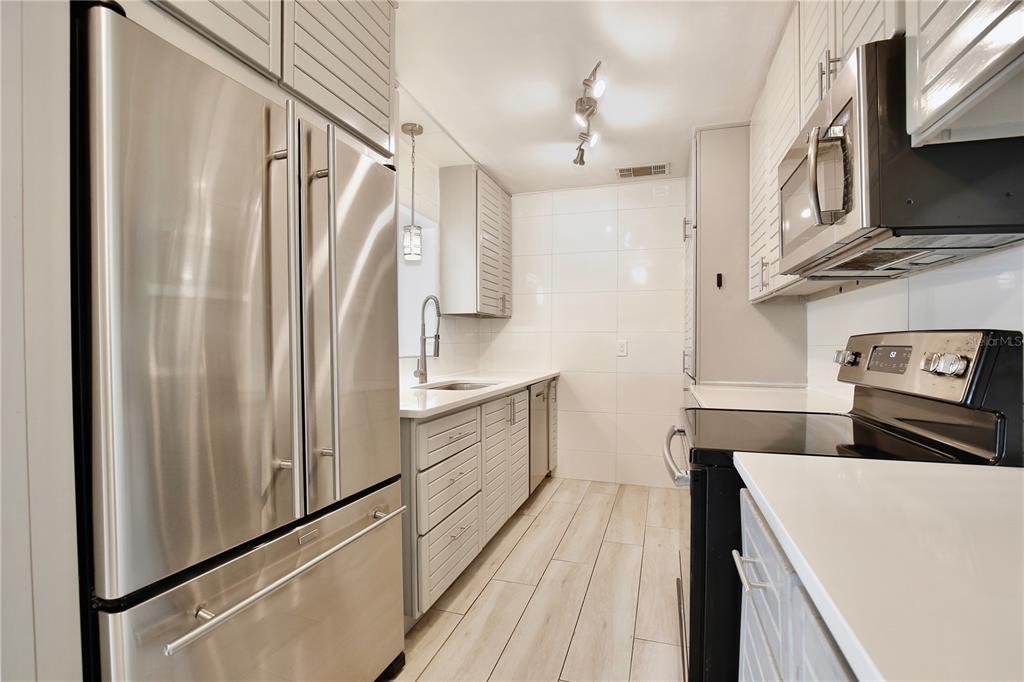 A galley kitchen features stainless steel appliances, light gray cabinetry, and white tiled walls — 2401 ALBERT LEE PARKWAY, WINTER PARK, FL