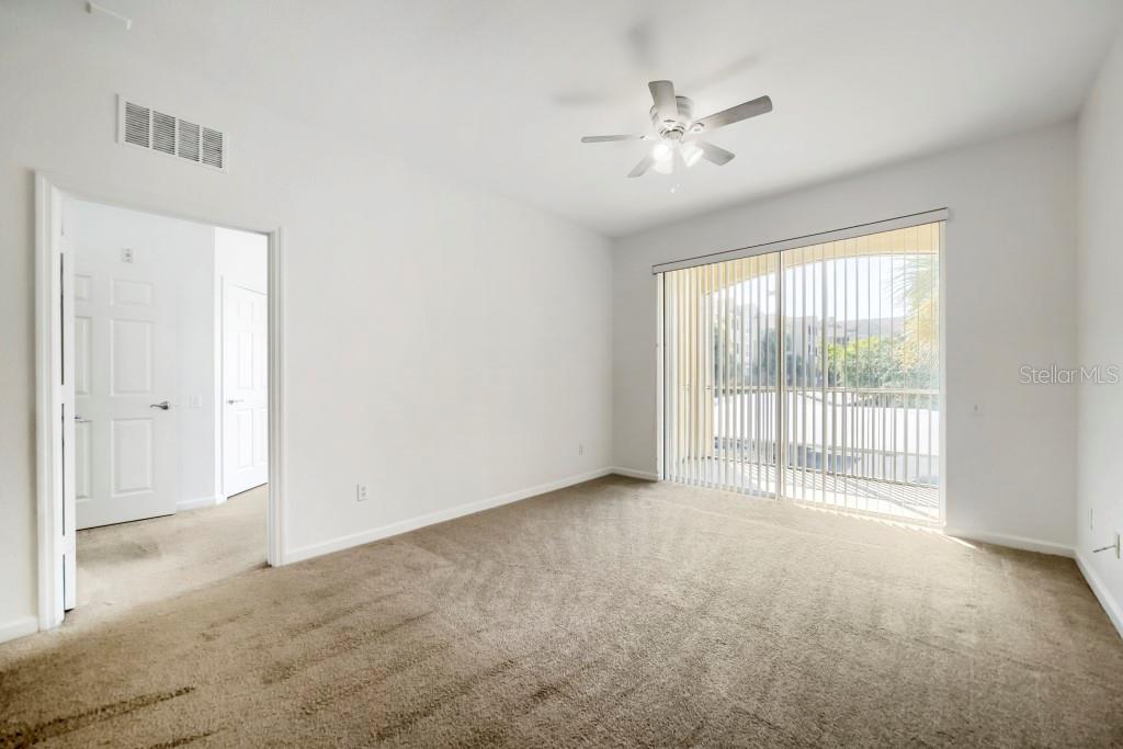 An empty bedroom features beige carpeting, white walls, a ceiling fan, and sliding glass doors — 6466 CAVA ALTA DRIVE UNIT 208, ORLANDO, FL