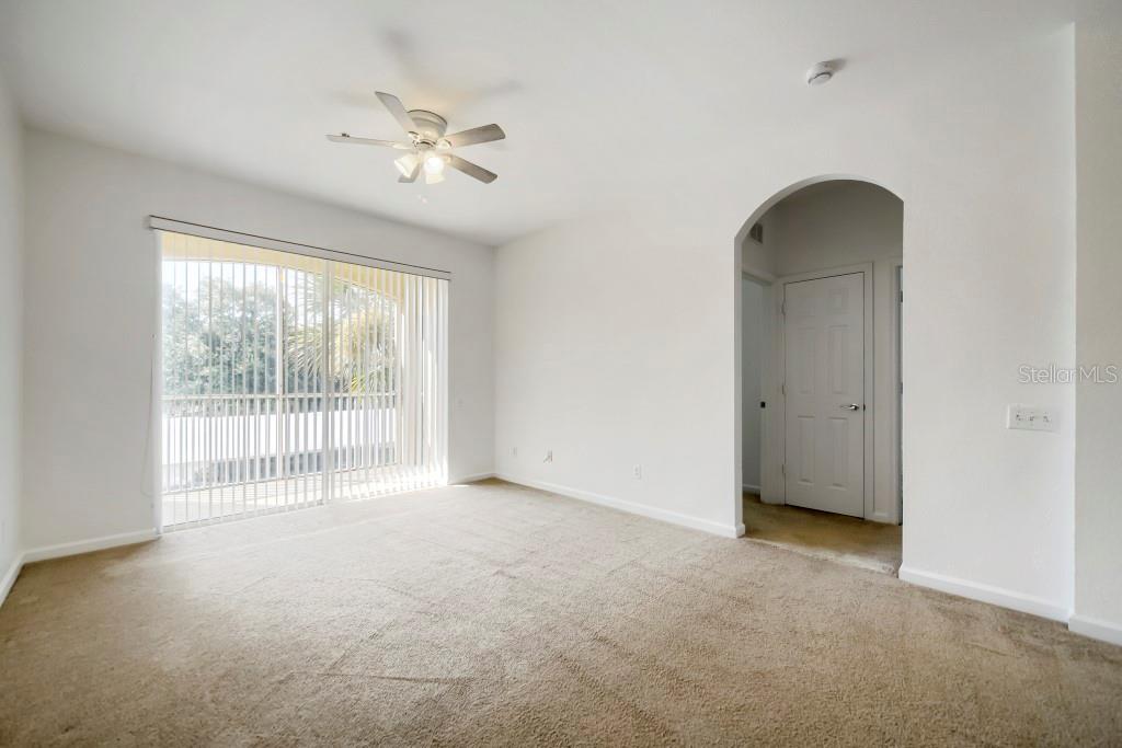 A carpeted room features a ceiling fan, sliding glass doors, and an arched doorway — 6466 CAVA ALTA DRIVE UNIT 208, ORLANDO, FL