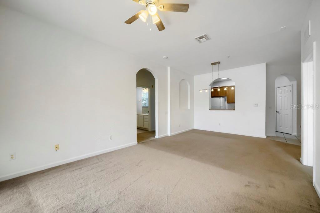 An empty living room with beige carpet, white walls, and an arched entryway — 6466 CAVA ALTA DRIVE UNIT 208, ORLANDO, FL