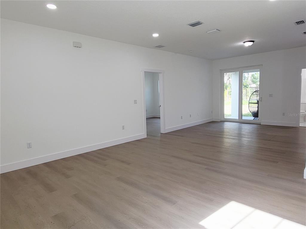 A spacious, empty room features light wood-look flooring, white walls, recessed lighting, and sliding glass doors — 1751 NANDINA COURT NW, PALM BAY, FL