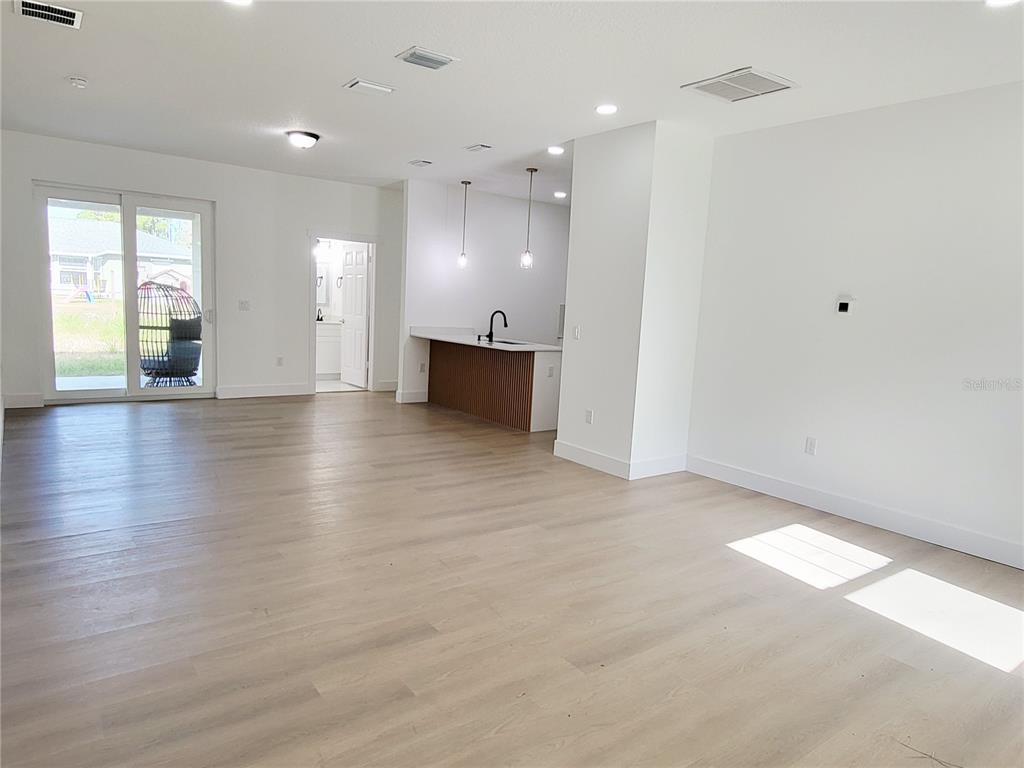An open-concept living area features light wood flooring, a kitchen island, and sliding glass doors — 1751 NANDINA COURT NW, PALM BAY, FL
